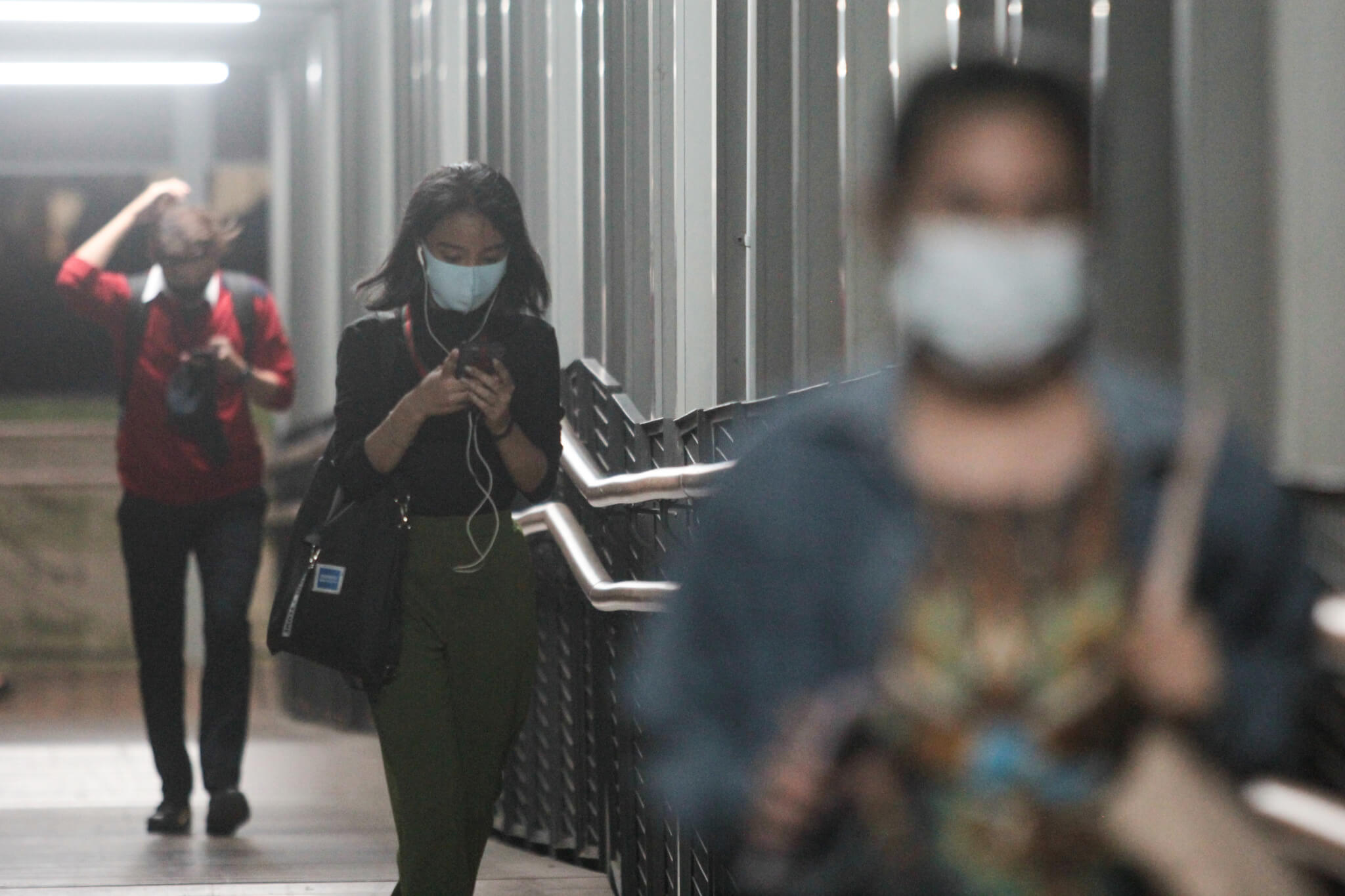Tiga orang sedang berjalan berjauhan di sebuah JPO sambil mengenakan masker